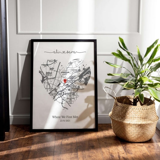 Framed heart-shaped city map wall art with custom text beside potted plant on wood floor